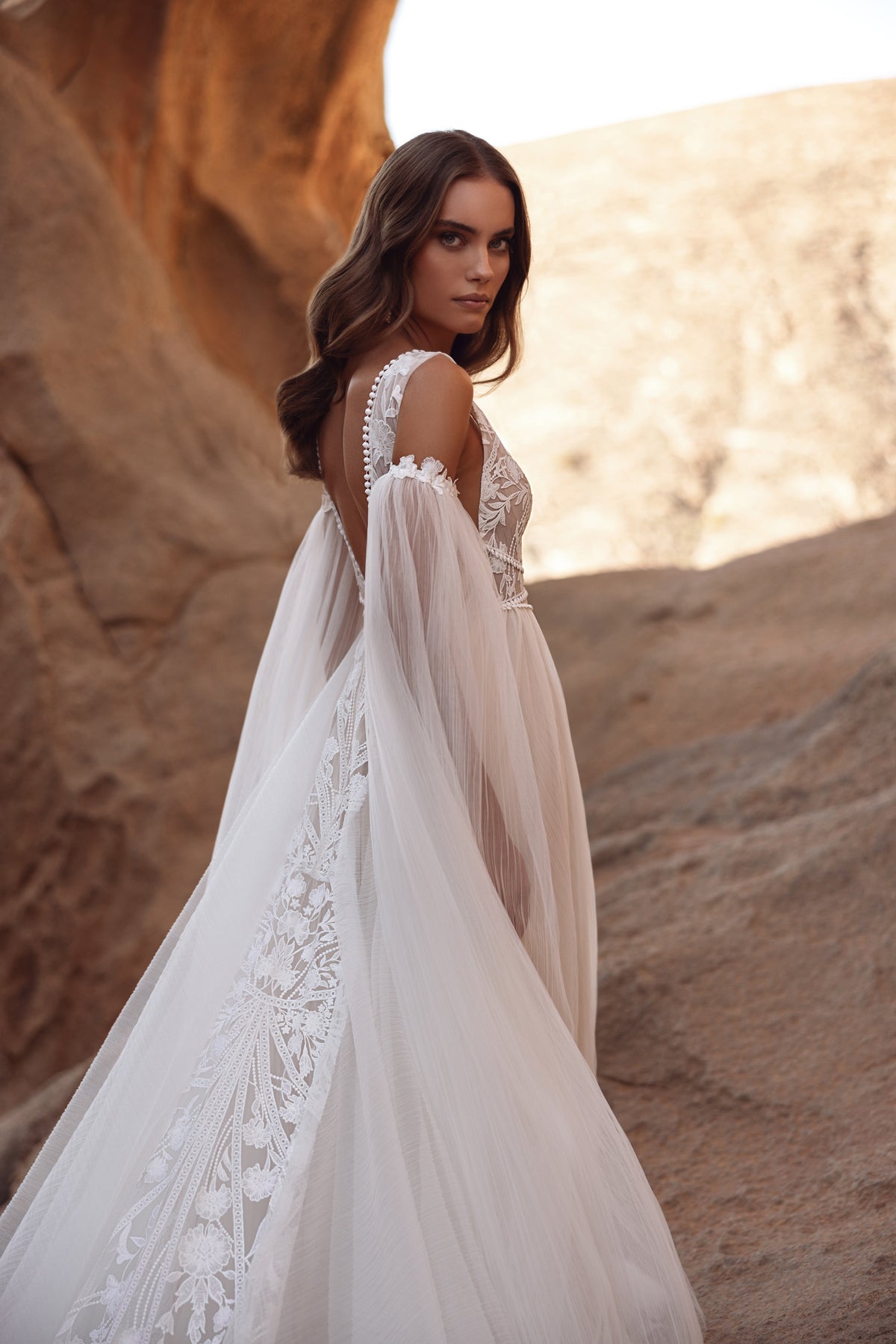 L’abito da sposa Salome, con profondo scollo a V e delicati dettagli in pizzo, valorizza la figura con eleganza leggera.
