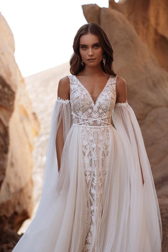 L’abito da sposa Salome, con spalle scoperte e lunghe maniche in tulle, unisce carattere boho e romantici dettagli in pizzo.
