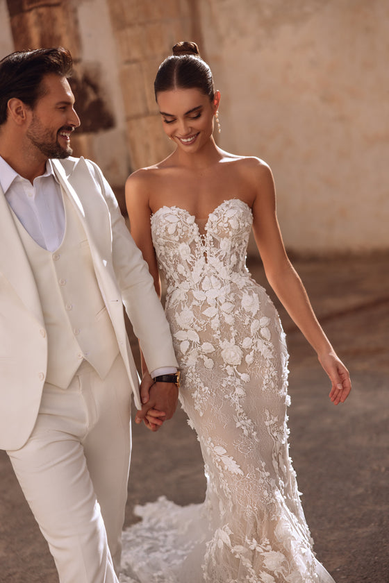 L’abito da sposa Sarifa, con schiena scoperta e strascico in pizzo floreale, unisce eleganza e sensualità.