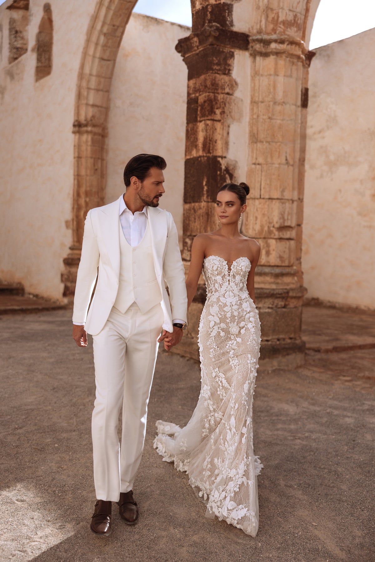 L’abito da sposa Sarifa senza spalline, con scollo a cuore e applicazioni floreali, esprime una raffinatezza romantica.