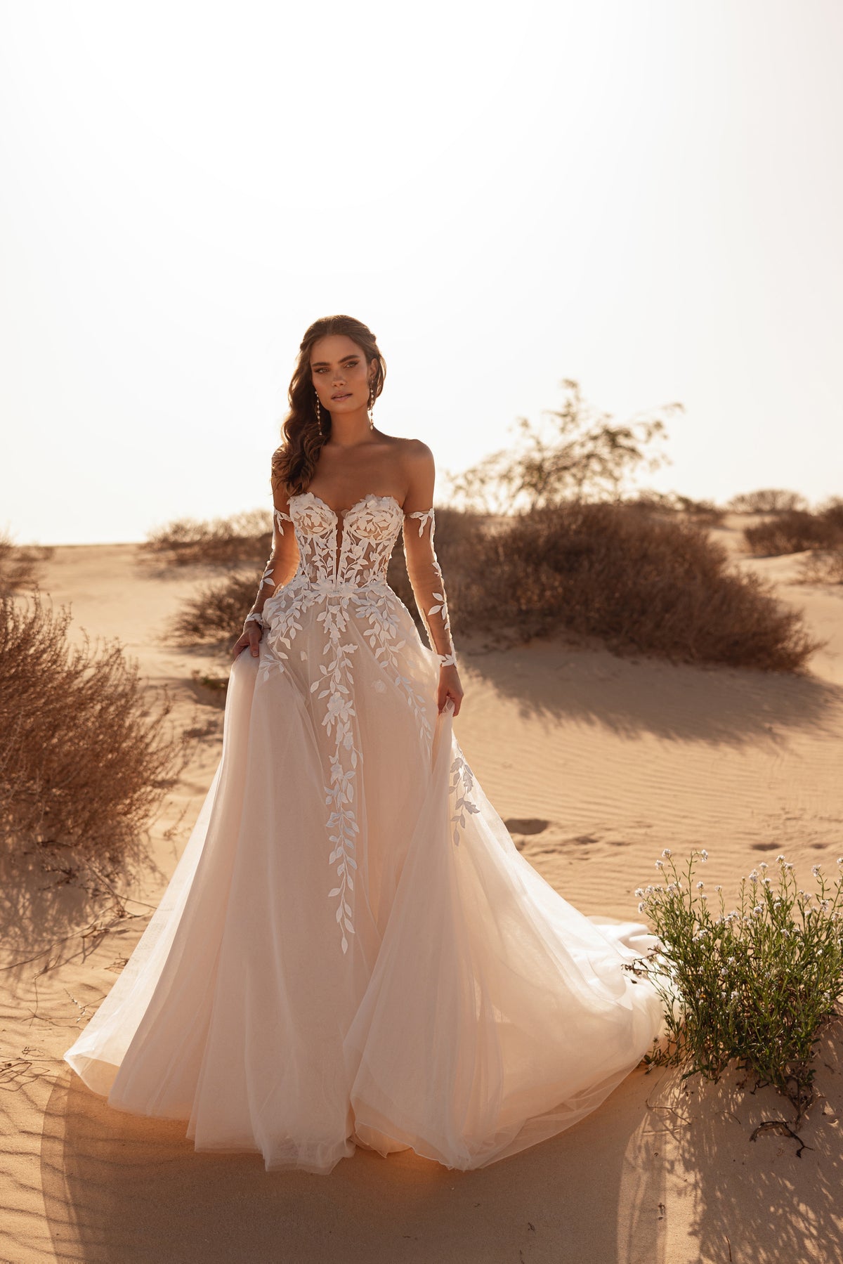 L’abito da sposa Tamara, con corsetto a spalle scoperte e strascico fluido in tulle, esprime romanticismo sotto il sole del deserto.