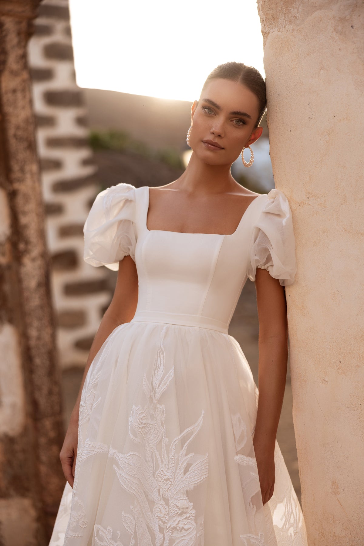 L’abito da sposa Vanilla, con maniche a sbuffo e scollo quadrato, propone un look d’ispirazione regale e contemporaneo.