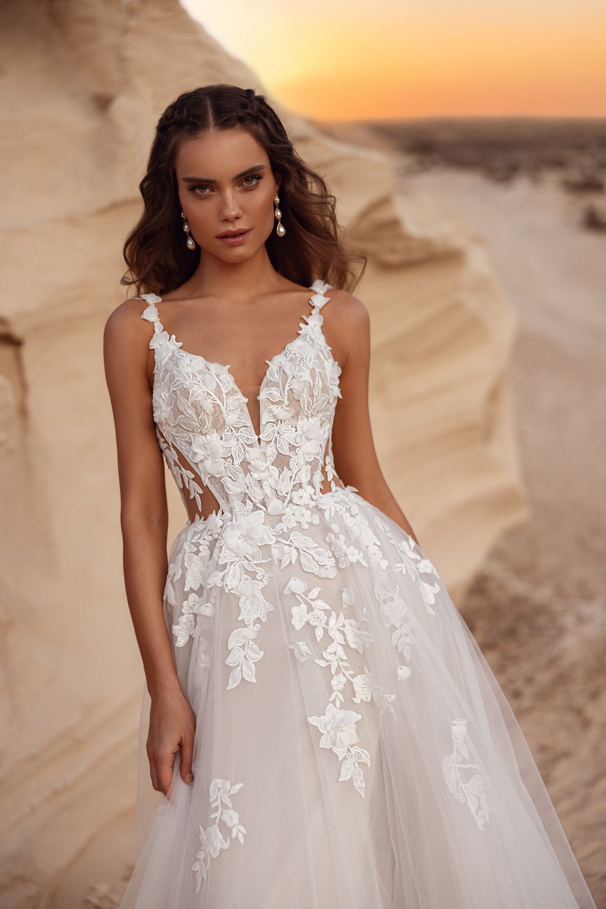 L’abito da sposa Zafira, con gonna in tulle e dettagli in pizzo floreale, accanto a uno sposo in completo beige, crea un’immagine sognante.