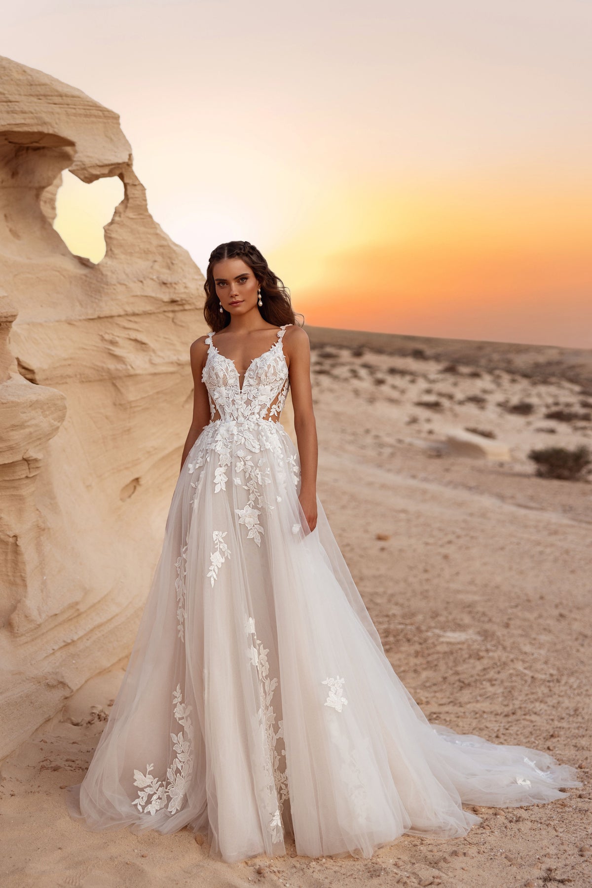 L’abito da sposa Zafira, con profondo scollo a V e applicazioni di pizzo floreale 3D, risplende sullo sfondo del tramonto nel deserto.